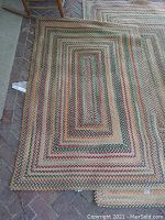 Close-up view of braided rug corner showing the braided texture and multicolor concentric rectangular geometric pattern.