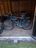 Full side view of blue mountain bike in shed, showing overall frame and tires flat.
