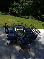 Full view of oval wrought iron patio table with clear glass top and six matching chairs on deck