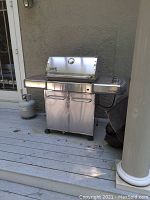 Full front view of Weber Genesis grill on deck, shows two-door cabinet, side shelves, propane tank and cover.