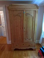 Full front view of the natural wood hutch showing two closed doors and one drawer beneath, with decorative carved details and scrollwork trim along the top.