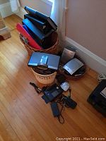 Wicker basket filled with plastic binders and office supplies on floor, with small electronics and cords nearby