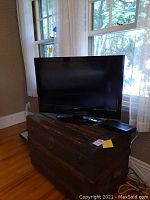 Vizio 32 inch flat screen TV placed on a wooden chest near window showing the full TV screen and stand.