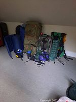 Photo of multiple backpacks, sleeping pads, and other camping gear arranged on floor under sloped ceiling