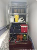 Metal wire 5-shelf unit standing with various items on shelves (not included).