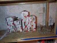 Multiple stacked boxes of La Rochere 1475 glassware and sample glasses on wooden shelf