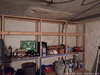 Shelf in basement with assorted items including pathway lights, storage bins with wire and rope, cans of paint, and other supplies.