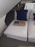Photo of the lounge chair seated with a large navy blue pillow and a packaged item on-seat, showing the beige fitted slip cover and the seat cushion