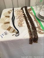 Five pieces laid out on a cloth-covered surface showing two decorative belts and three necklaces.