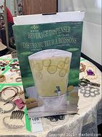 Box showing product name 'Acrylic Beverage Dispenser' with image of the dispenser filled with a lemon beverage.