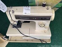 Off-white Kenmore 6 sewing machine with visible wear, showing stitch selector controls and power cable on a beige base with storage compartment underneath.