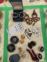 Photo showing the full collection of assorted earrings including gold-tone hoops in a velvet box, wooden drops, silver-tone hammered drops, black bead clusters, black shiny round earrings, cream decorative drops, gold-tone clip-ons, red bead drops, and a single earring.