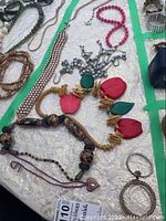Photo showing six pieces of jewelry laid out on a lined cloth including necklaces and bracelets with varied designs and colors.