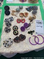 Top view of assorted earrings spread on a cream-colored fabric background showing various styles and colors including clip-on and pierced earrings.