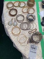 Photo showing multiple bracelets arranged on cloth-covered surface including bangles, cuffs, and chain linked styles in various metallic finishes.