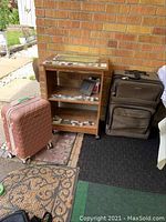 Laminate wood cabinet on wheels with two suitcases, showing wear and tear, outdoor setting on a mat and tile floor.