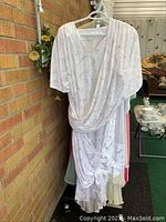 Front view of a light-colored night robe with draped front, hanging on a hanger outdoors near a brick wall.