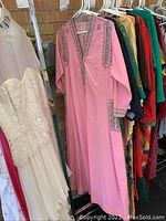 Photo showing a pink long dress robe with silver embroidery on neckline, cuffs, and pockets, hanging among other colorful robes.