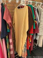 Closet rack showing various robes mostly hanging together, with beige pleated asymmetrical robe front and center.