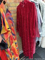 Photo showing three robes hung on a rack including a red velvet-textured robe, a vibrant multicolored robe, and a neutral fur-like robe.