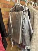 Metallic silver long sleeve top, hanging on a white hanger, medium size, displayed near a brick wall with other clothing.