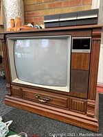 Front view of RCA Color Trak TV in wooden cabinet showing large convex screen, control panel, speaker, and tape deck along with detailed carved wood base and brass handle.