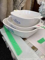 Three stacked white CorningWare baking dishes displaying blue cornflower pattern, no lids shown.