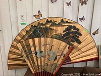 Two fans partially open against a wall with butterfly decorations, showing Asian-style paintings.