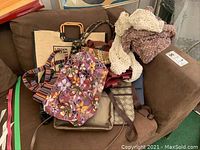 Full lot of various women's handbags, purses, and scarves arranged on a brown couch.