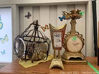 View of the clock lamp, metal and glass chandelier, and musical box candle holder arranged side by side on a shelf.