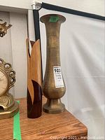 Two vases on a wooden surface: a tall brass vase with engraved designs and a tapered wooden vase with a decorative open petal top and two-tone finish.