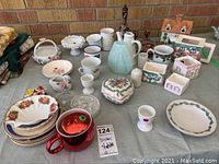 Wide view of mixed dishes, cups, bowls, decorative ceramic items, including floral plates and a pale blue ceramic pitcher arranged on a table.