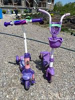 Front view of two children's scooters, showing one with a front basket and both with sturdy three-wheel design.