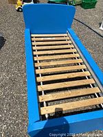 Blue IKEA toddler bed frame with wooden slats visible. The frame is on an outdoor gravel surface, showing some paint chipping.