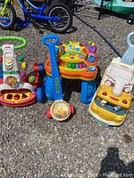 Photo showing all 4 children's activity toys including walker, learning table, popper, and ride on truck on gravel