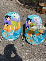Both infant bouncers side by side outdoors, showing colorful fabric seats with animal patterns; one bouncer has attached activity bar with toys.