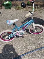 Side view of blue 16-inch kids bicycle with white tires and pink rims, showing frame, seat, chain guard, and front tire.