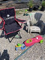 Photo showing black and red folding camping chair with Canada logo, small gray Adirondack chair, and pink children's golf set on gravel ground.