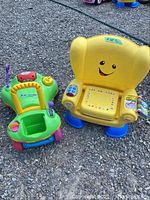 Yellow Fisher Price toddler reading chair and green walker/rider toy side by side on an outdoor surface.