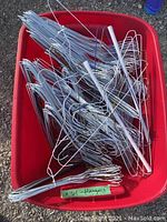 Large red bucket filled with numerous silver metal wire coat hangers. Hangers appear bent in places but generally in usable condition.