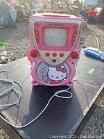 Front view of Hello Kitty karaoke machine showing screen, buttons, speakers, and microphone input.