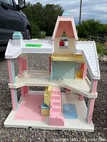 Front-facing view of plastic Barbie doll house showing three stories, stairs, and open room layout.