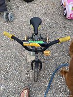 Top view of boys Huffy bike showing padded handlebar cover and yellow grips, pedals, seat and frame detail, on gravel surface.