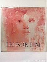 Front cover of the art book showing the dust jacket with artwork of a female face in pinks and reds and the title 'LEONOR FINI'.