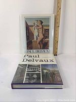Two Paul Delvaux art monograph books stacked and standing, showing cover art and size comparison with ruler.