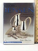 Front cover of hardcover book Georg Jensen: A Tradition of Splendid Silver showing silver pitcher, jug, sugar bowl, and jewelry.