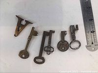 Top down view of six old skeleton keys and decorative letter 'A' on a white surface with ruler for scale.