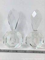 Pair of clear faceted vintage glass perfume bottles with matching stoppers beside a ruler for size reference.