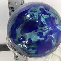 Side angle showing the spherical shape, color pattern, and glass loop for hanging. Includes rulers for size reference.