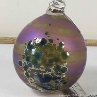 Side view of the hand blown glass ball showing iridescent purple gold colors with bubble design and hanging loop.
